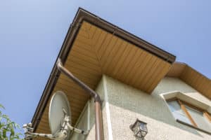 Bottom view detail of new modern house top with decorative lamp and satellite dish on stucco walls, plastic attic window, gutter pipe system on blue sky copy space background. Real estate concept.